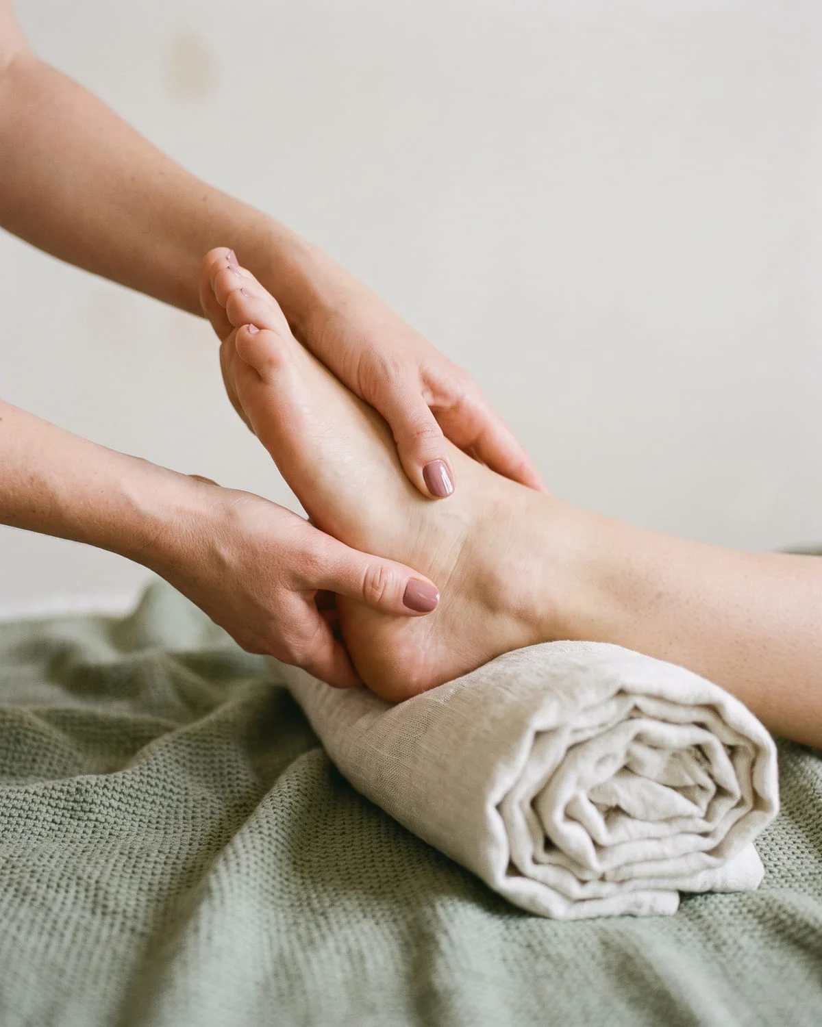 Des mains pressent doucement la plante d'un pied nu posé sur une serviette en lin