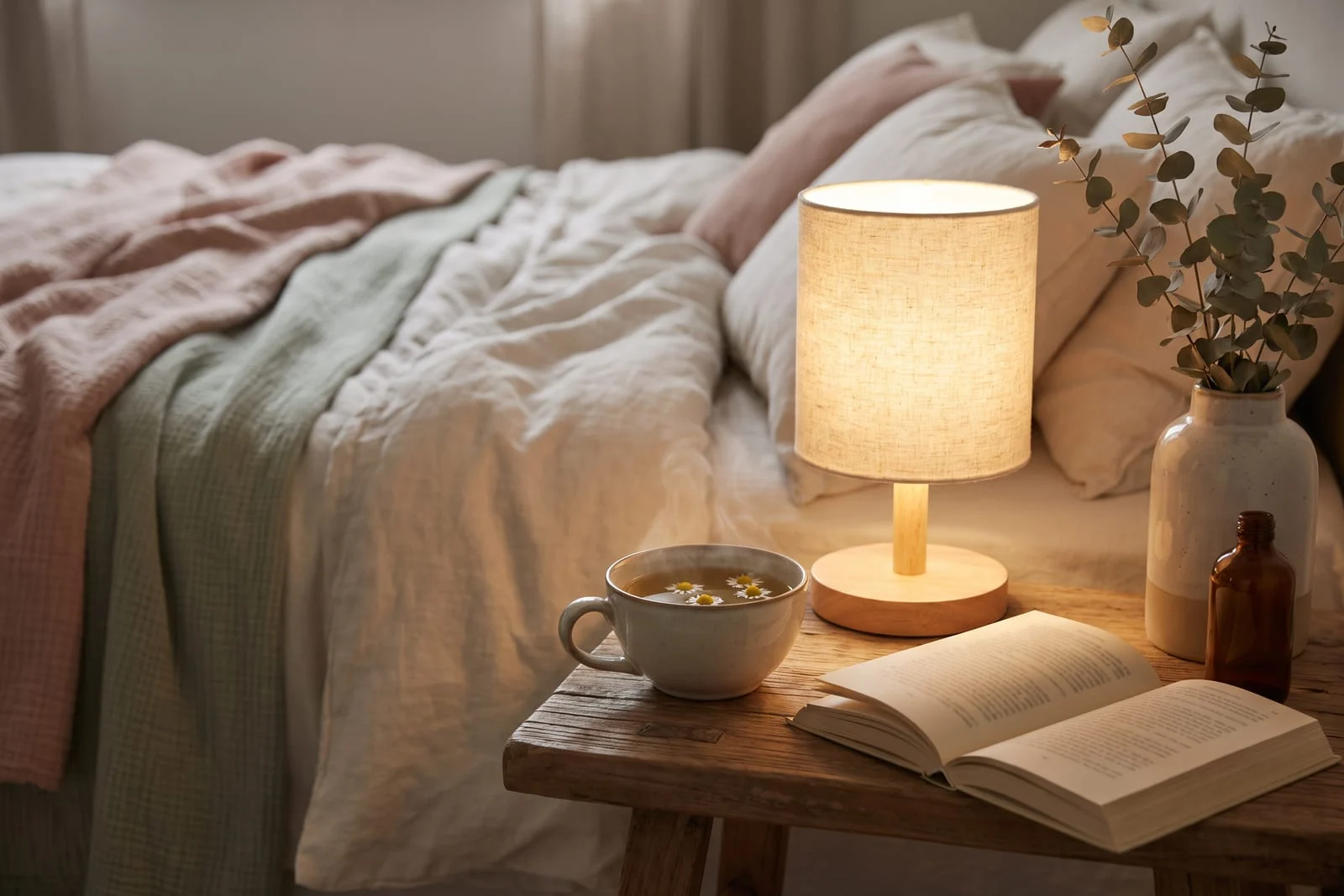 Table de chevet avec une infusion de camomille, un livre et une lampe